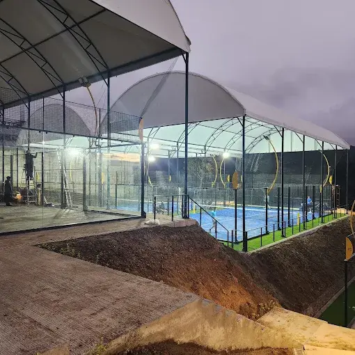 Covered padel courts in Guatemala during installation, with the arched roof structure lit at night